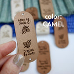 Hand holding Faux leather tag in color camel or beige, with the text Crochet by custom name and holes for attaching to crocheted or knitted items. And more tags with personalized texts and logos on the background.