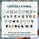 35 options of symbols to use on tags for crocheted and knitted items. In this image there are washing instruction symbls, yarn balls, sheeps, hearts and other nature symbols like stars, moons and trees.